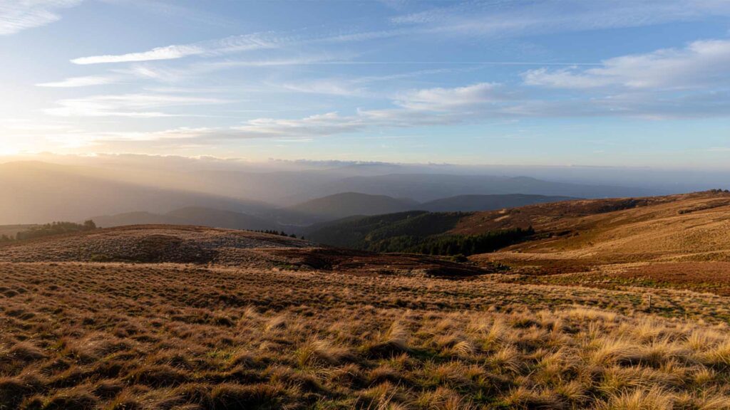 Golden hour light illuminating rolling hills and distant mountains in a natural landscape scene.